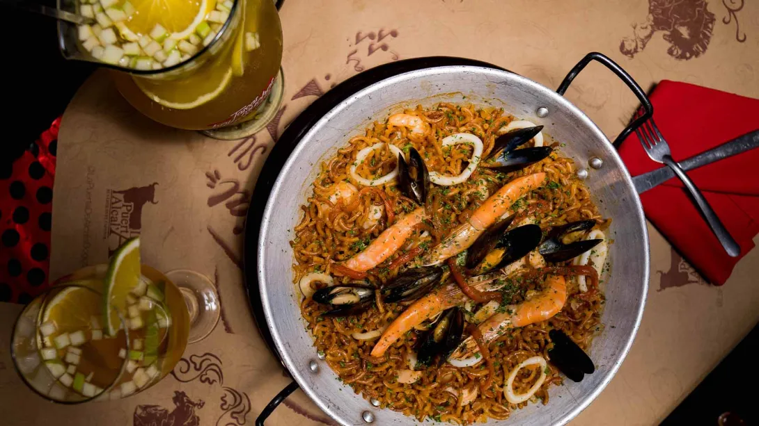 Fideuá de mariscos en una paellera, acompañada de refrescante sangría, lista para una deliciosa comida.