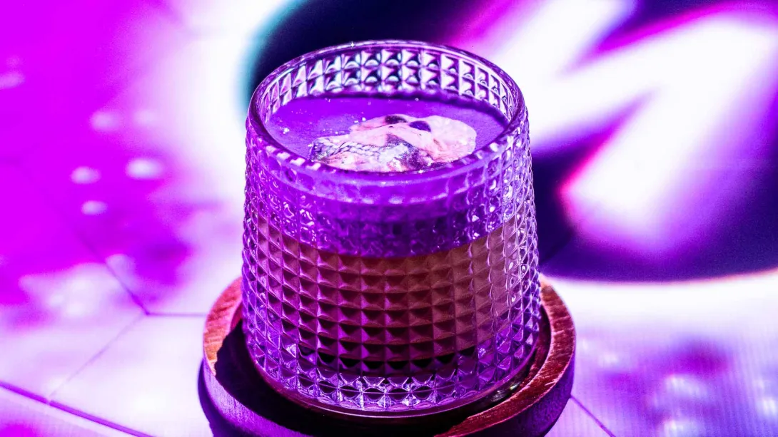 Una bebida misteriosa en un vaso texturizado, con una decoración en la superficie bajo luz violeta.