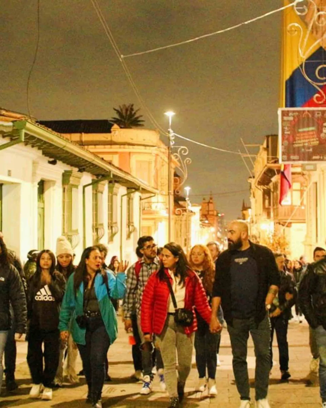 Grupo de personas hombres y mujeres jóvenes camina de noche por entre las calles de La Candelaria. 