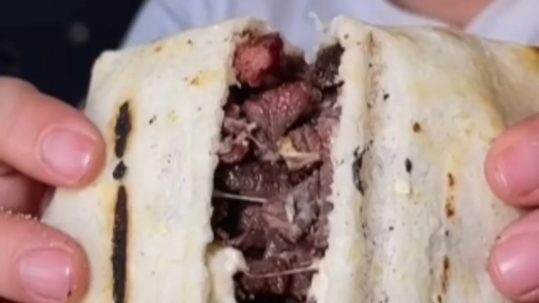 Primer plano de un trozo de arepa blanca abierta en la que se ven trozos de carne.