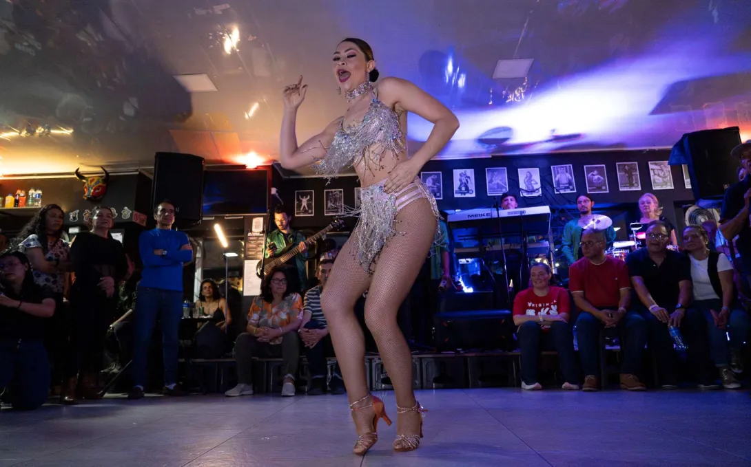  Una mujer con un taje de bailarina blanco baila frente a varias personas.