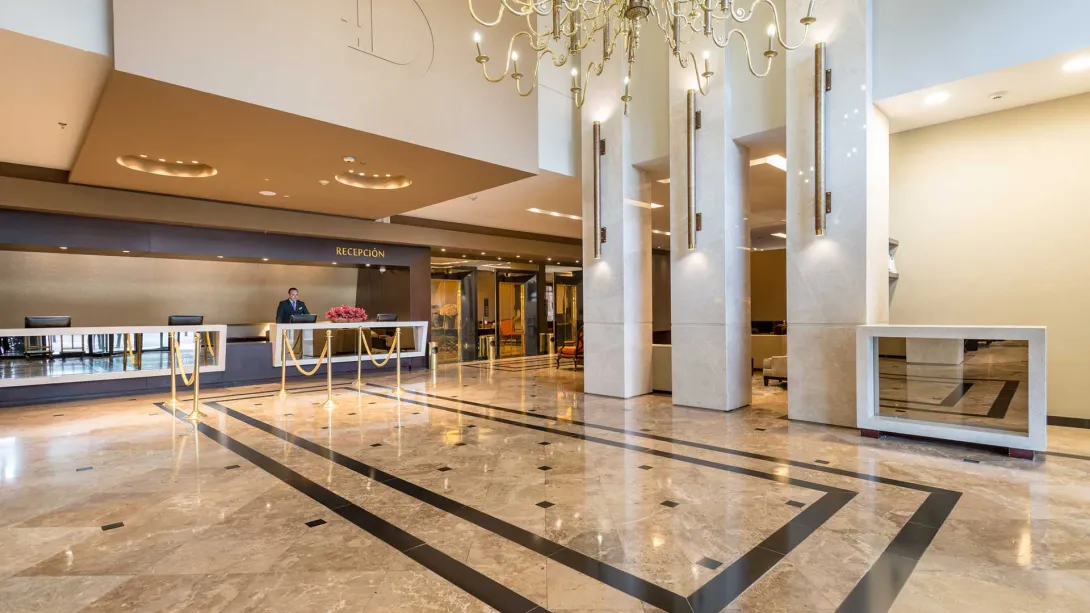  Lobby:Lobby amplio con recepción iluminada, mármol en pisos, columnas altas, candelabro dorado y espejos que brillan al fondo.