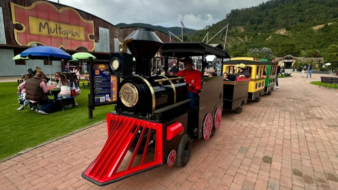A miniature train in a playground. There are people around it, and a mountain can be seen in the background.