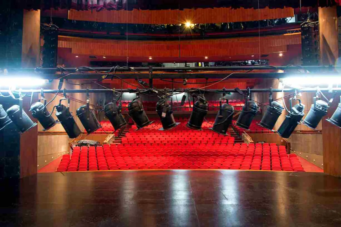 Primer plano de focos de luz en un teatro. Al fondo se observan las sillas en el escenario.