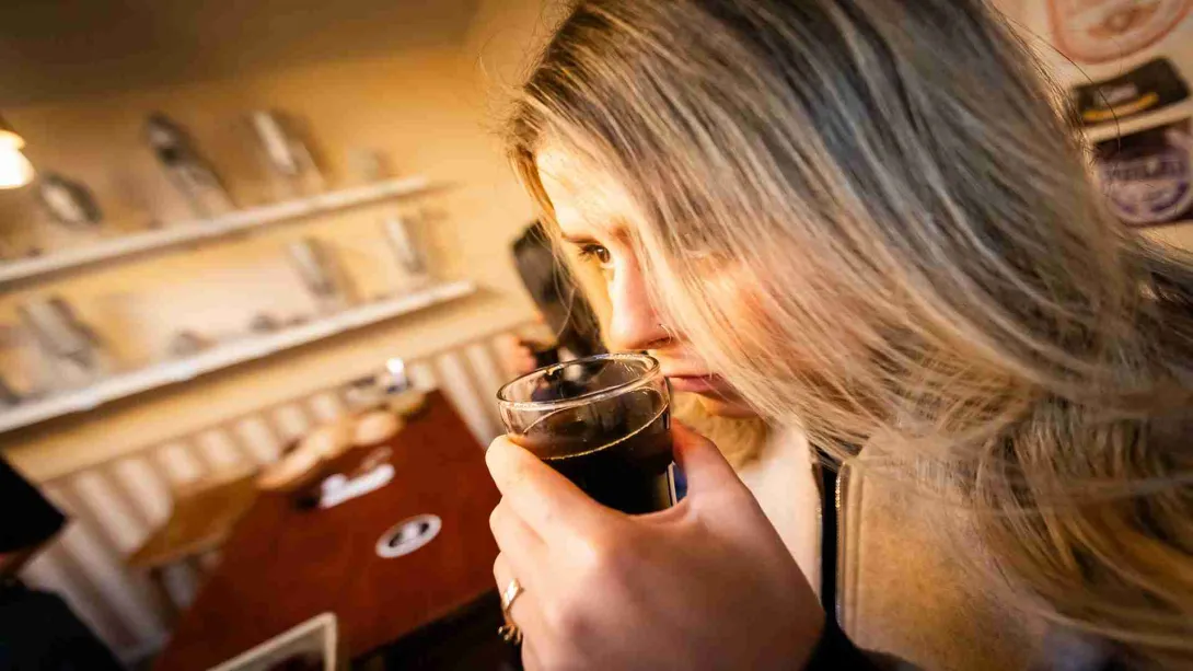 Una mujer joven huele el contenido de una copita parece que con cerveza.