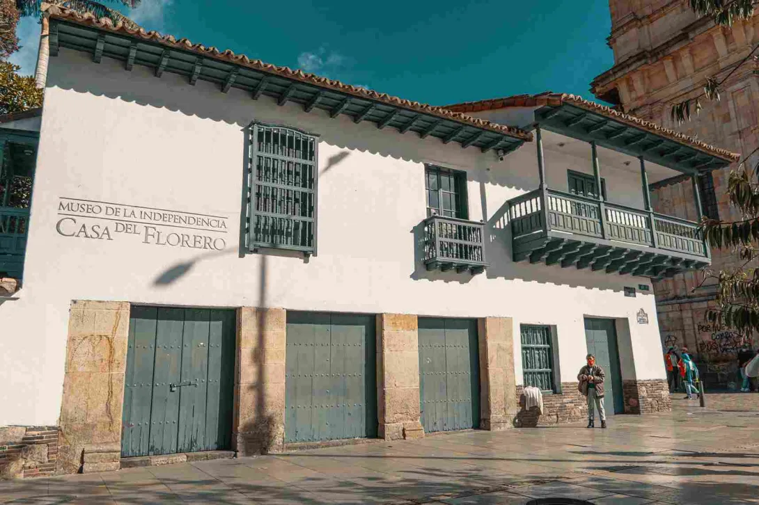 Fachada de casa antigua de estilo colonial con balcones y puertas de color verde. Resalta una leyenda en una de las paredes blancas, que dice: “Museo de la Independencia - Casa del Florero”.