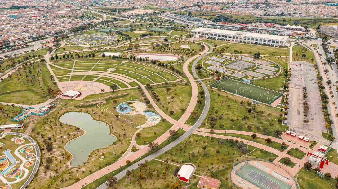 Plano general visto desde arriba de un parque gigantesco donde hay canchas deportivas, amplias zonas verdes y un gran lago.