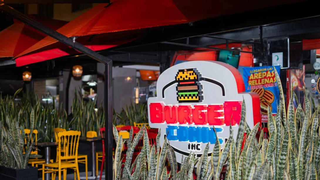 Un letrero luminoso de "BURGER COMIC INC" con una hamburguesa pixelada brilla por la noche en la entrada del restaurante.