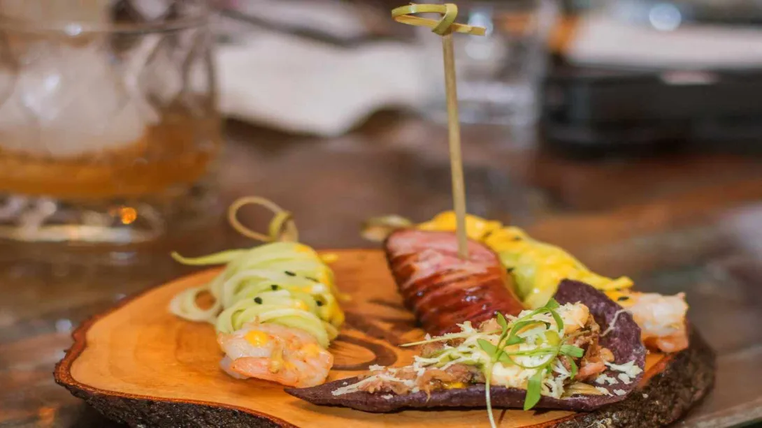 Tabla de madera con una selección de variados y coloridos aperitivos gourmet y un cóctel. 