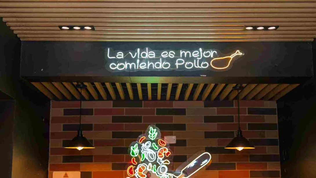 Un letrero de neón con la frase "La vida es mejor comiendo pollo" ilumina el techo de madera del restaurante.