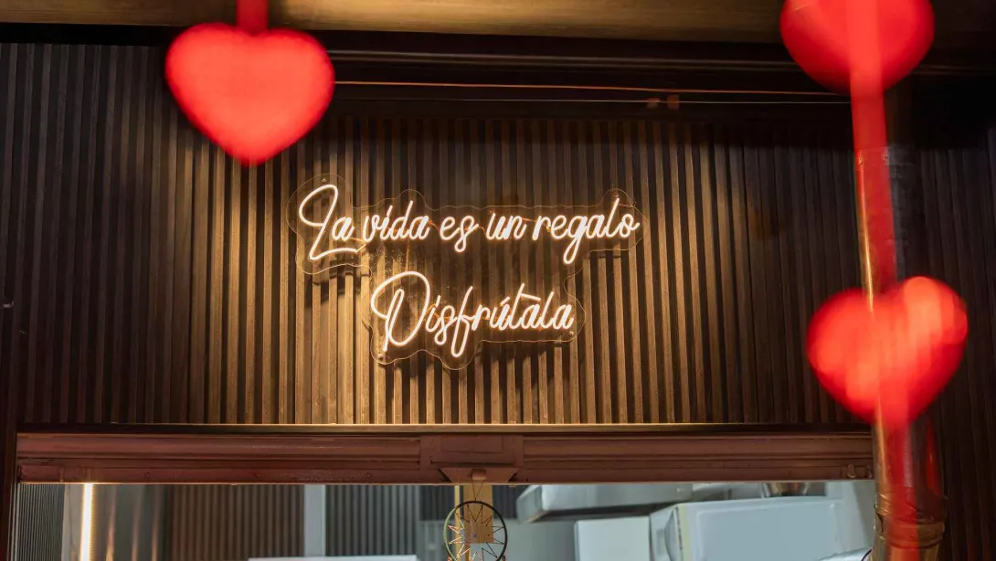 Letrero de neón con la frase "La vida es un regalo, disfrútala" sobre una pared de listones de madera oscura.