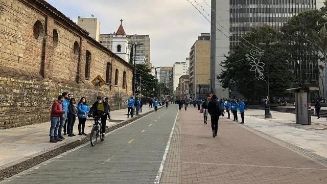 En el centro, la Carrera Séptima luce organizada y abierta, con un carril para bicicletas y amplios espacios para peatones. Personas caminando, conversando y un ciclista en movimiento reflejan un ambiente tranquilo y dinámico, enmarcado por edificios modernos y árboles que aportan equilibrio al paisaje urbano.