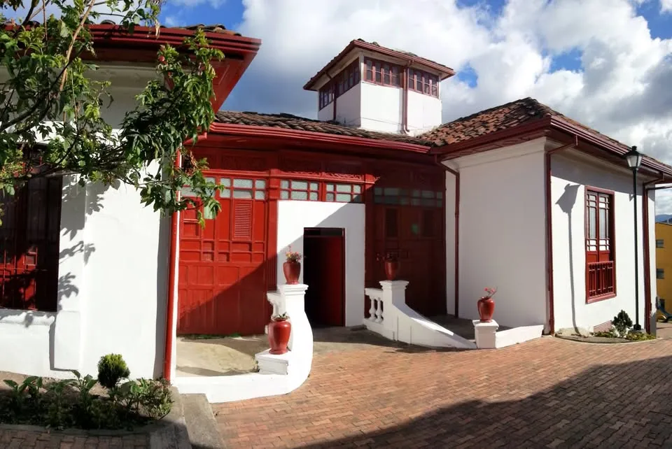  Fachada de casa estilo colonial donde las paredes son blancas y las puertas y ventanas rojas.