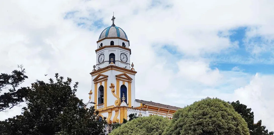  Vista de la torre principal de una iglesia en la que se observa un campanario y varios relojes. En la punta de la figura en forma de óvalo hay una cruz metálica.