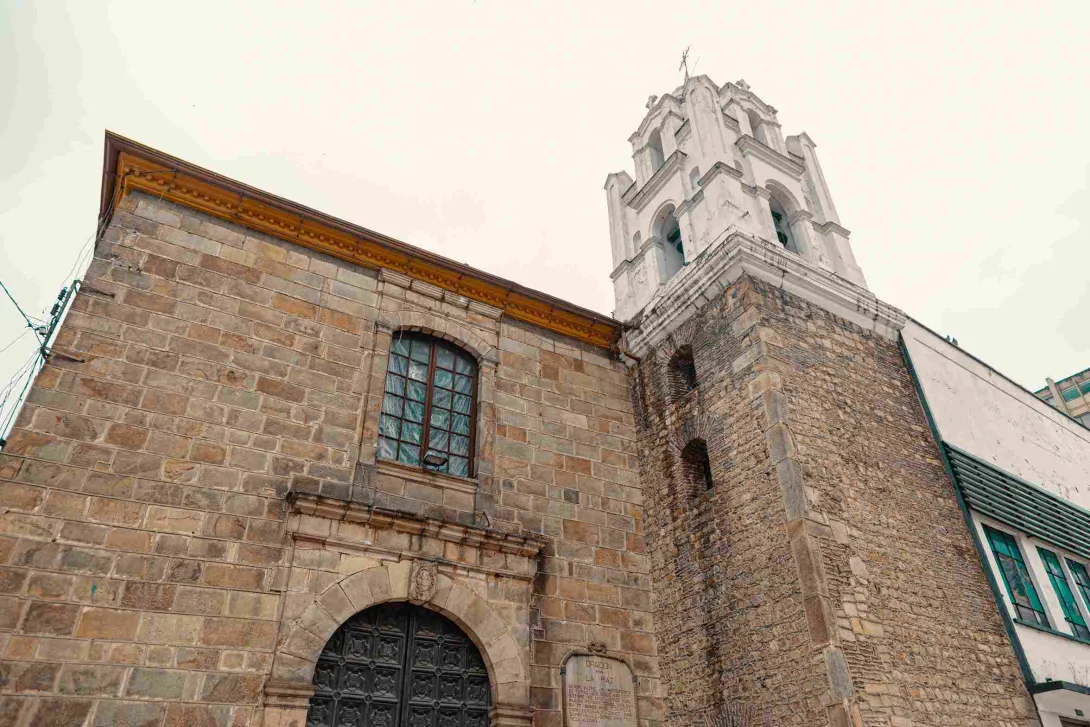 Vista desde abajo de la fachada de la iglesia en piedra y concreto blanco. Se destaca su alta torre blanca.
