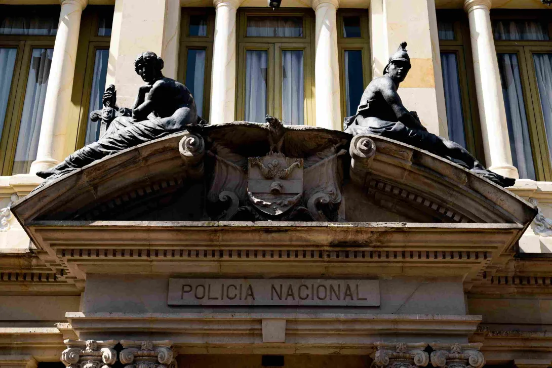 Close-up of a building facade showing two stone figures of soldiers seated on the roof, the Colombian coat of arms, also in stone, and the inscription "National Police."