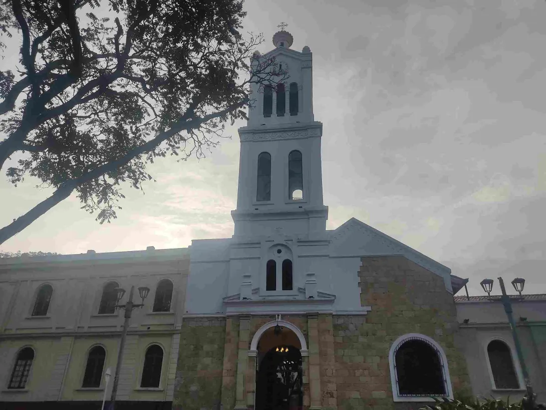 Front view of the church facade, highlighting its structure of stone and white concrete, the tall bell tower, and its arched entrance.