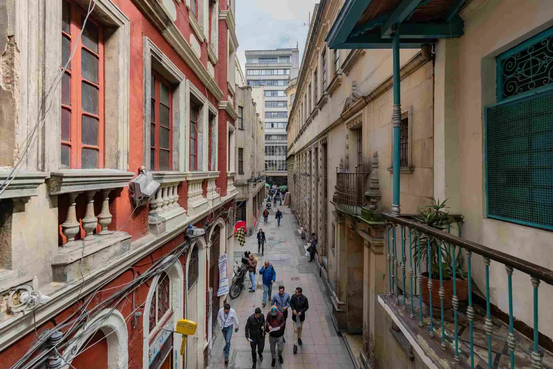 Aerial view of a narrow, alleyway-style street between old buildings, where several people are walking.