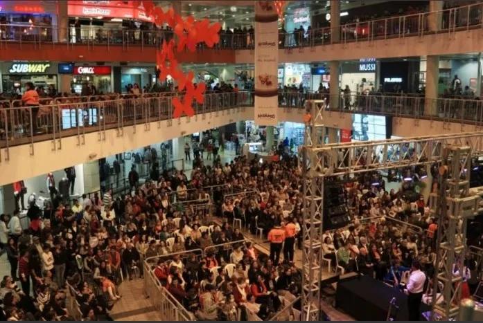 Interior de centro de comercio en el que se observan tres pisos con locales comerciales repletos de personas.