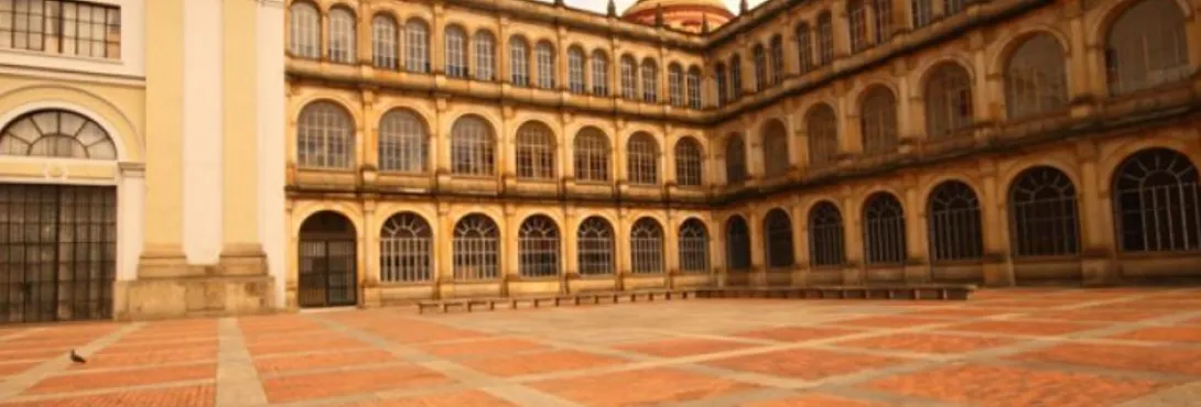  Patio amplio de un edificio histórico con arquitectura colonial, rodeado por una estructura de varios pisos con arcos repetidos y grandes ventanales. El suelo es de ladrillo dispuesto en patrón geométrico y el espacio está casi vacío, con una atmósfera tranquila. 