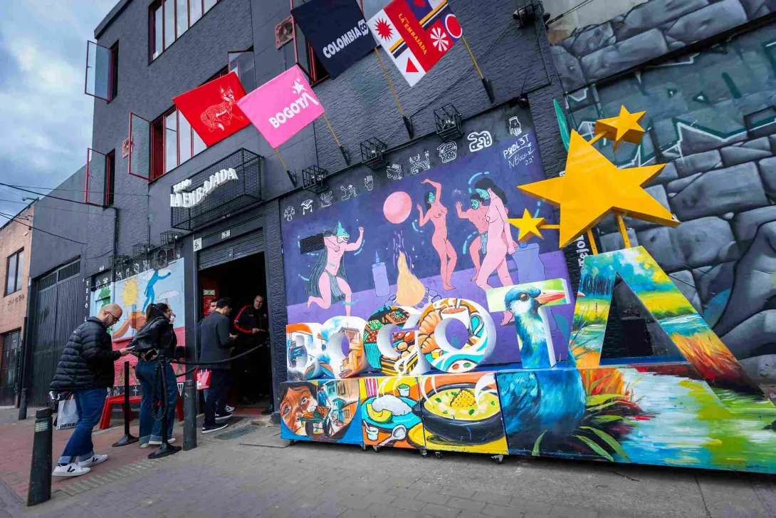 Fachada de edificio gris con vibrante arte callejero y una gran instalación de letras que deletrea "BOGOTÁ" en la acera.