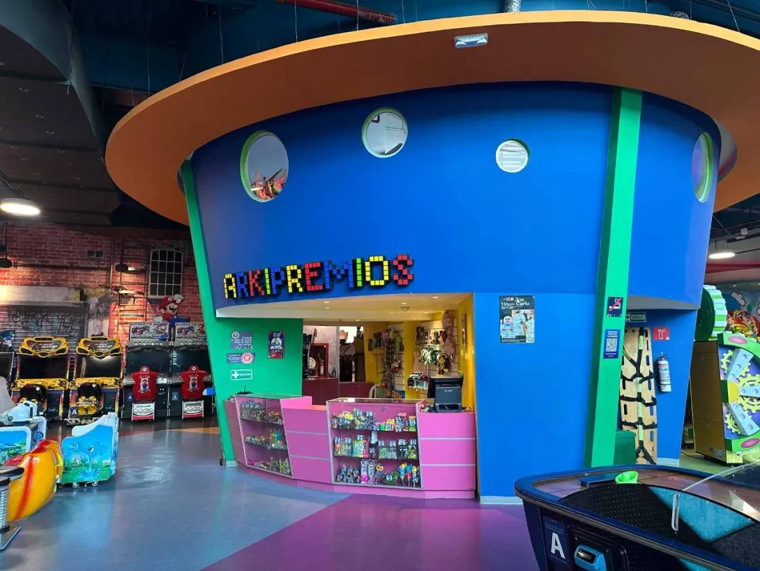 Mostrador de premios en un parque de entretenimiento interior, con fachada colorida y máquinas de videojuegos alrededor.