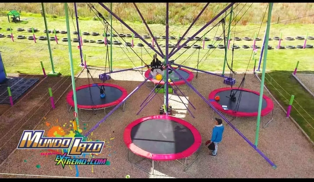  Estructura de trampolines circulares conectados por cuerdas en un parque al aire libre, con personas saltando y supervisando la actividad.