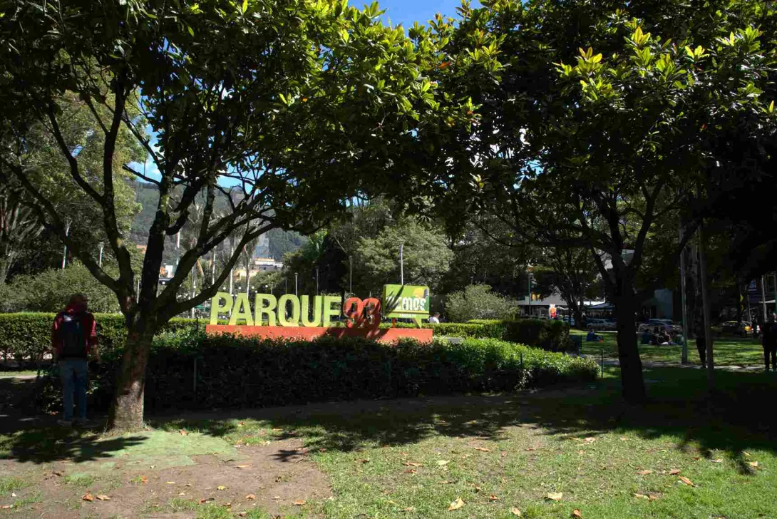 Letrero de “Parque 93” rodeado de árboles y jardines, en un espacio público al aire libre.