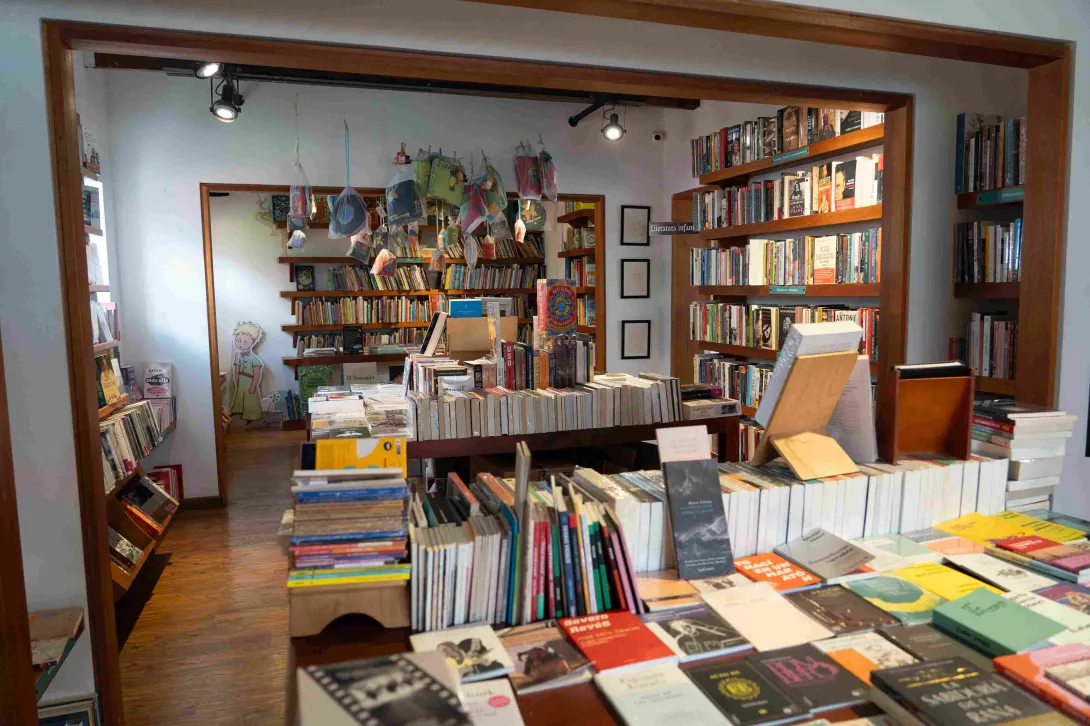 Interior de una librería con estanterías de madera llenas de libros, mesas de exhibición y una sección infantil al fondo decorada con ilustraciones.