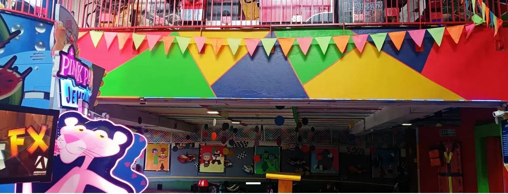 Fachada colorida de una zona de juegos interior con banderines, ilustraciones y letreros luminosos.