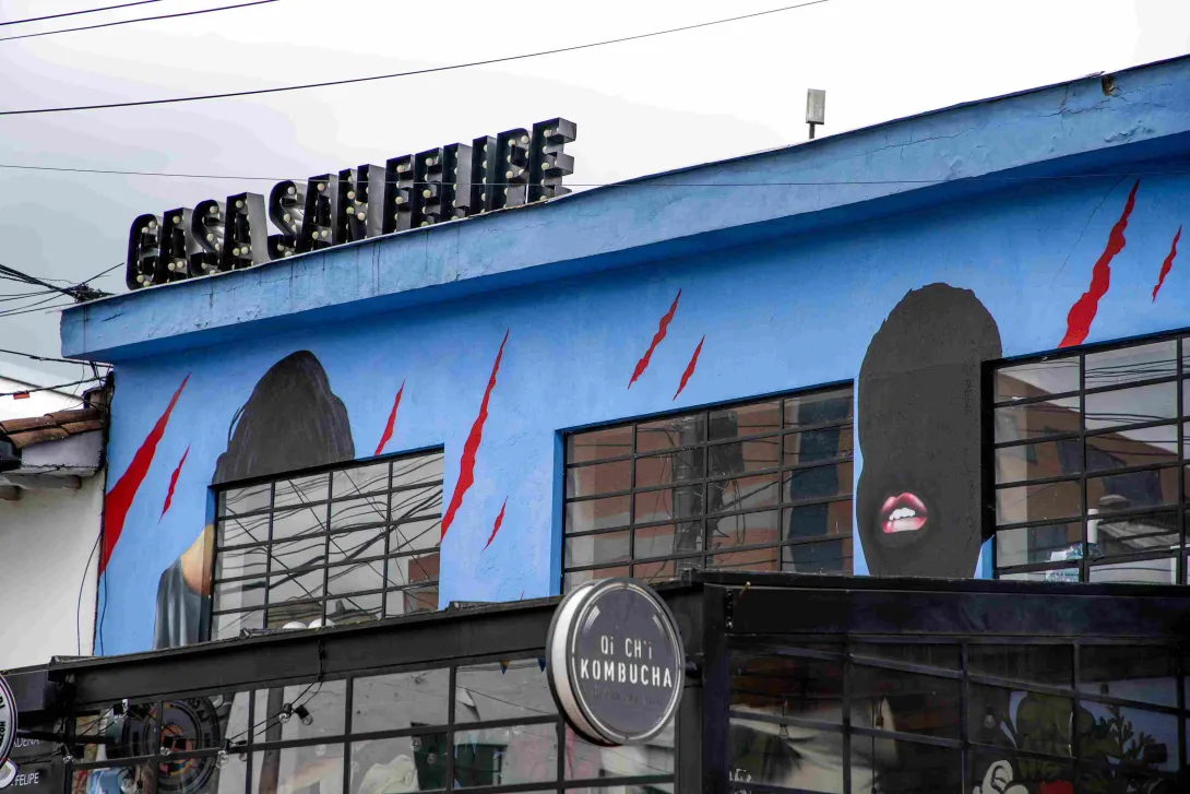 Facade of Casa San Felipe with an urban mural on a blue background depicting human silhouettes and red lines; the name of the place is visible at the top.