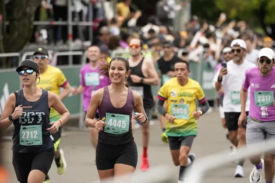 A group of runners participates in a race, with a smiling woman in the foreground and cheering spectators in the background.