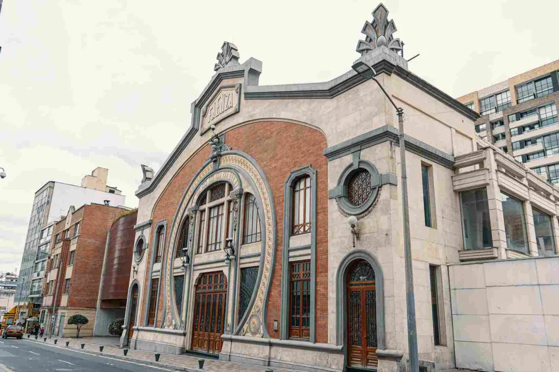 La imagen muestra un edificio de estilo arquitectónico clásico con detalles ornamentales, donde se combinan muros de ladrillo y piedra clara. Su fachada destaca por arcos decorativos y elementos artísticos en la parte superior, evocando un carácter cultural e histórico.