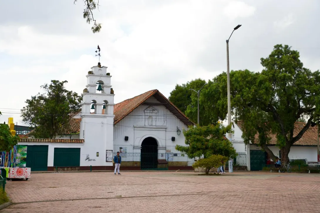 Iglesia colonial blanca con campanario en la plaza principal de Bosa, rodeada de árboles y espacio abierto.