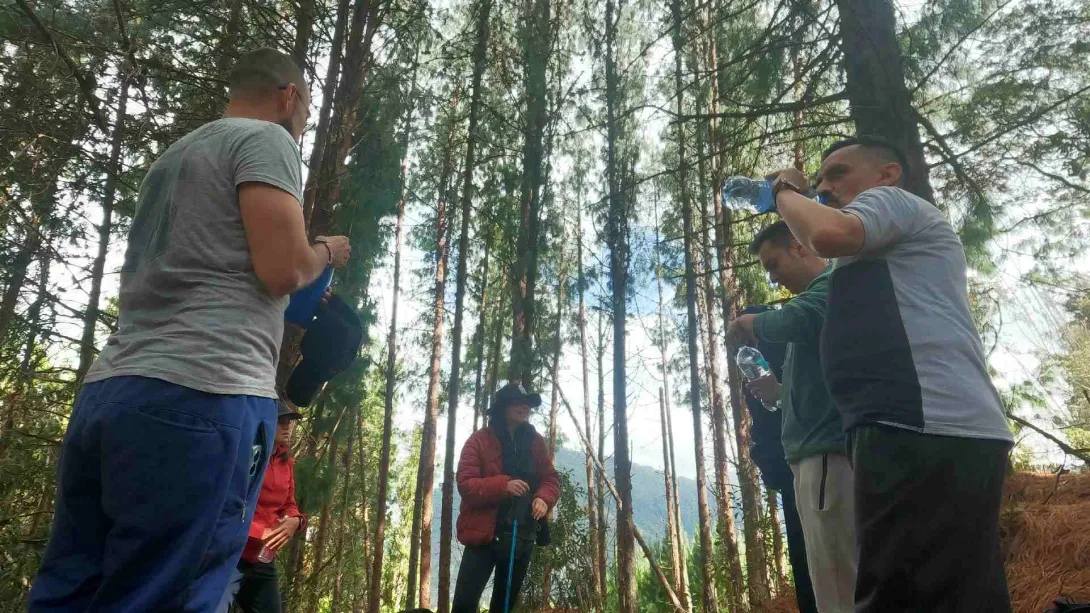 Grupo de personas en un bosque hace una pausa durante una caminata, hidratándose y conversando entre árboles altos y luz natural filtrada.