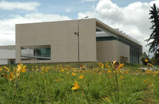 Vista exterior de un moderno complejo acuático rodeado de jardines y flores amarillas, cuya arquitectura contemporánea se integra con el entorno natural y los espacios verdes que lo rodean.