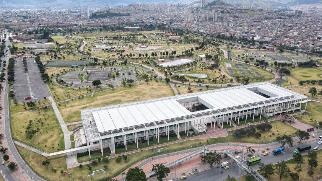 Aerial view of the El Tunal Happiness Center (CEFE) and its urban surroundings in southern Bogotá. The image shows ample green spaces, pedestrian walkways, sports facilities, and recreational areas integrated with the complex's modern infrastructure, surrounded by the city's extensive urban fabric and the mountains in the background.