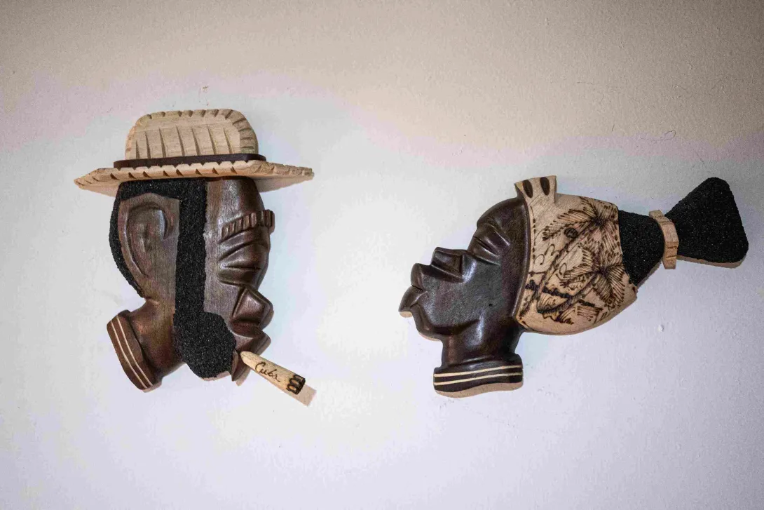 Dos máscaras artesanales de madera, decoradas con sombreros y detalles tallados, exhibidas sobre una pared blanca como parte de una colección cultural.