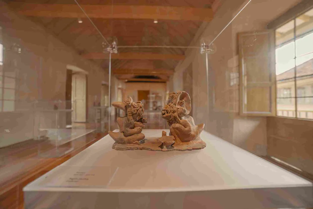 Pieza arqueológica de cerámica exhibida en una vitrina de museo, en una sala con pisos de madera, techos altos y luz natural.