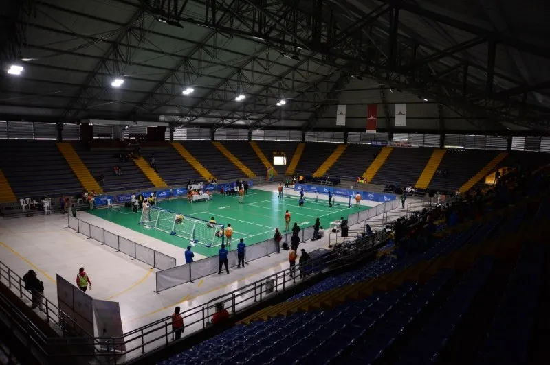 Interior view of the Palacio de los Deportes in Bogotá during a badminton tournament, showing several courts in use and stands surrounding the sports venue.