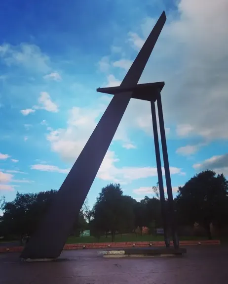 Monumental steel sculpture located at the High-Performance Center in Bogotá, surrounded by green areas and framed by a partly cloudy sky.