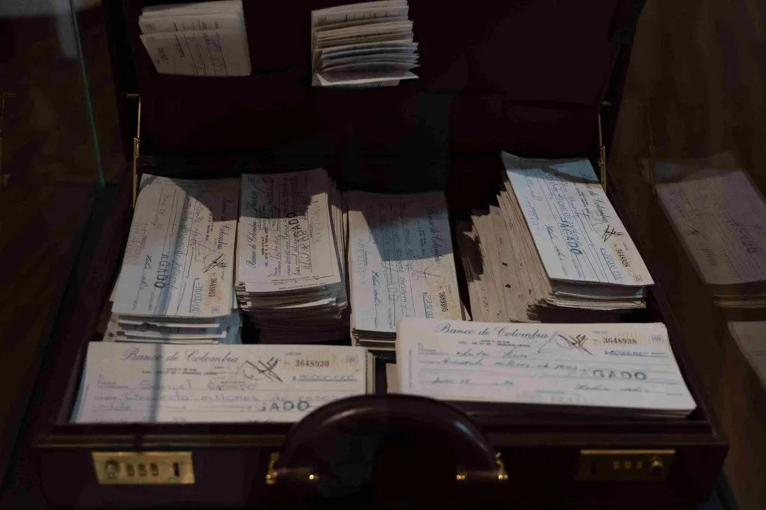 Maletín abierto con numerosos cheques antiguos del Banco de Colombia, exhibidos como documentos históricos en un espacio museístico.