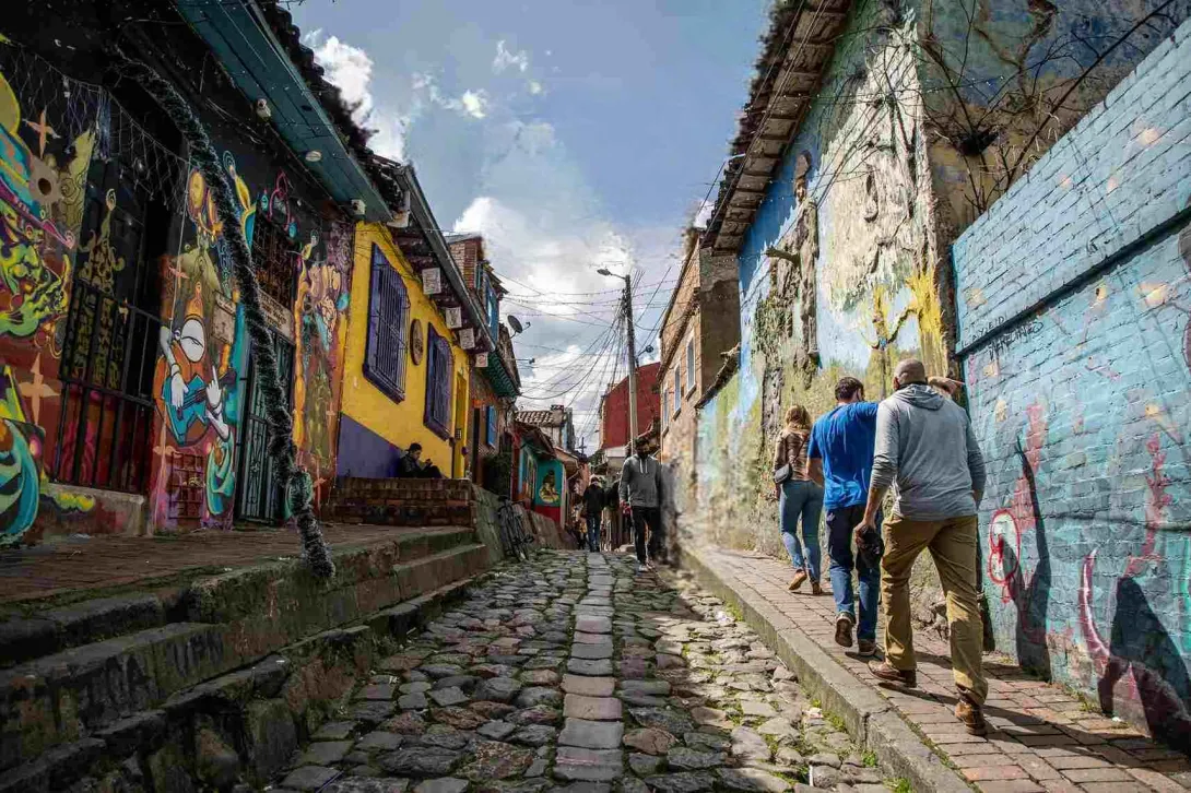  Callejón del Embudo en La Candelaria, con visitantes recorriendo su calle empedrada, rodeada de casas coloridas y muros decorados con arte urbano.