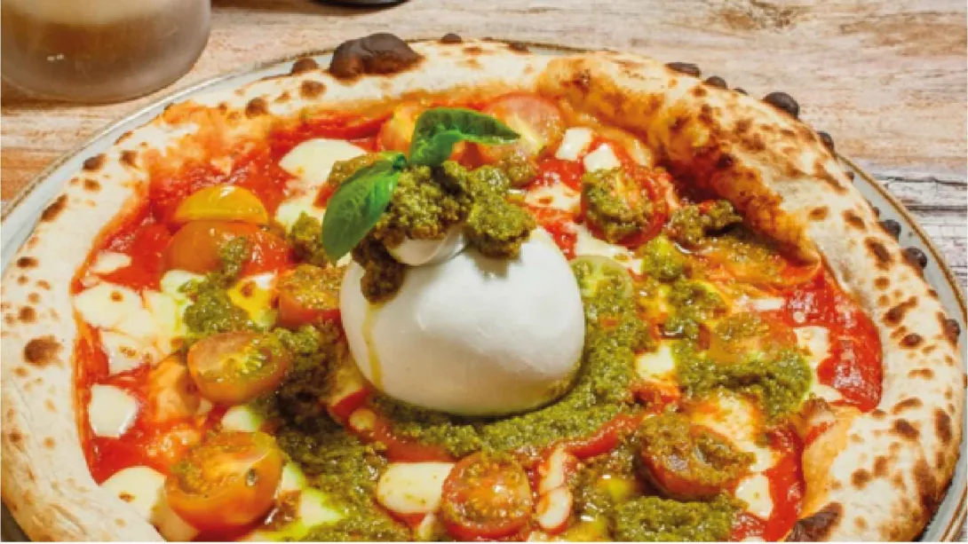 Pizza artesanal de masa crujiente con salsa de tomate, pesto, tomates cherry y una gran burrata fresca en el centro.