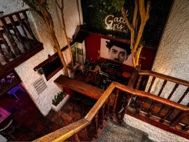 Interior de El Gato Gris, con escaleras de madera, decoración colonial y un retrato en la pared.