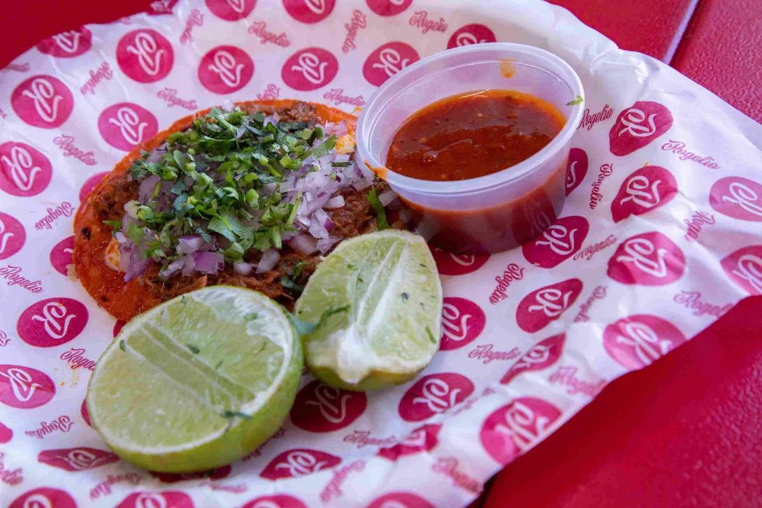Tacos de birria con cebolla, cilantro, limón y salsa roja.