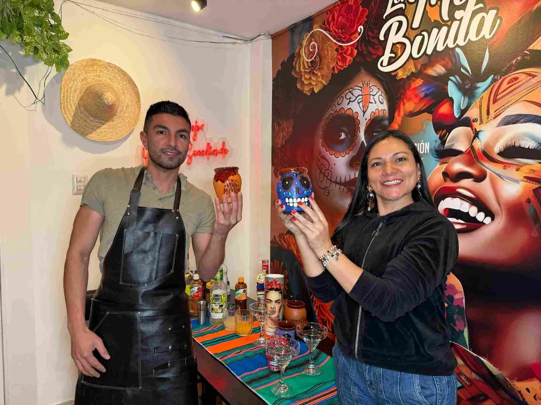Dos personas sostienen vasos decorativos durante una experiencia gastronómica de inspiración México-Colombia.