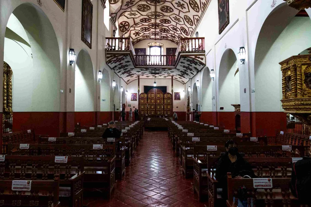 Interior de la Iglesia de San Juan de Dios, con naves laterales, bancas de madera, retablos dorados y un elaborado techo colonial decorado.
