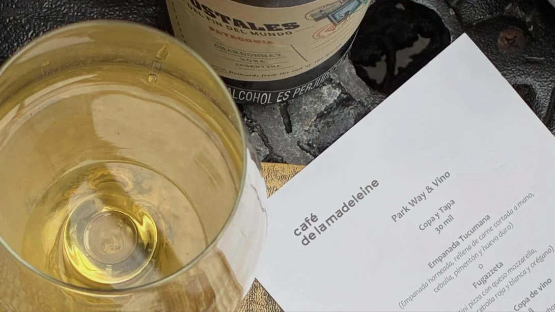  Copa de vino blanco junto a la carta de Café de la Madeleine, en una mesa que invita a descubrir su propuesta gastronómica.