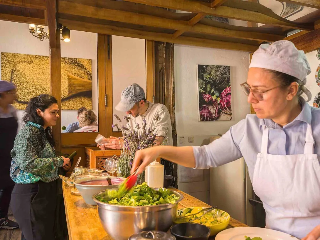 Cocineros preparan alimentos frescos en un ambiente cálido y artesanal, con ingredientes vegetales dispuestos para su elaboración.